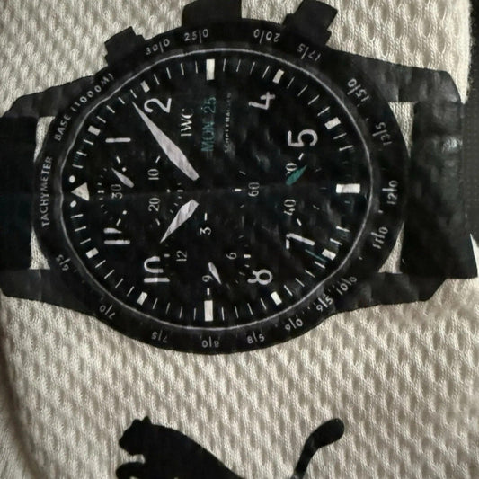 George Russell 2024 Qatar GP Race Gloves F1 Mercedes black wristwatch with a textured black strap, featuring a black dial with white Arabic numerals, white hands, and a black bezel with white tachymeter markings. The watch is photographed flat on a textured off-white fabric background with a black Puma logo printed below.