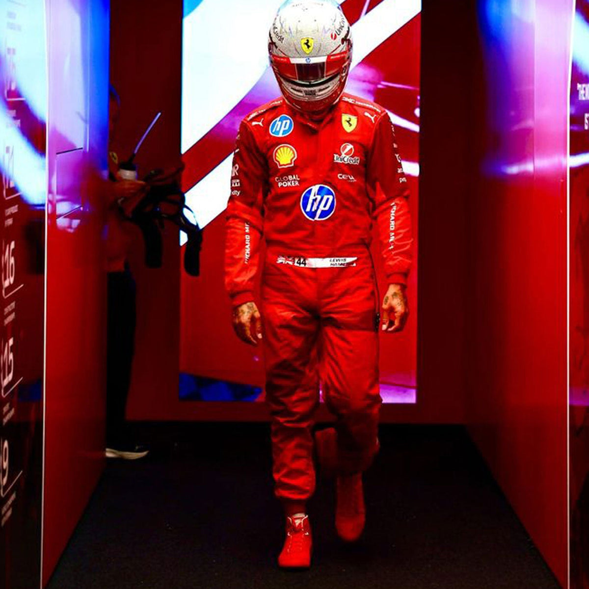 Lewis Hamilton 2025 F1 Race Suit Ferrari Las Vegas GP with various sponsor logos in a red-themed room.