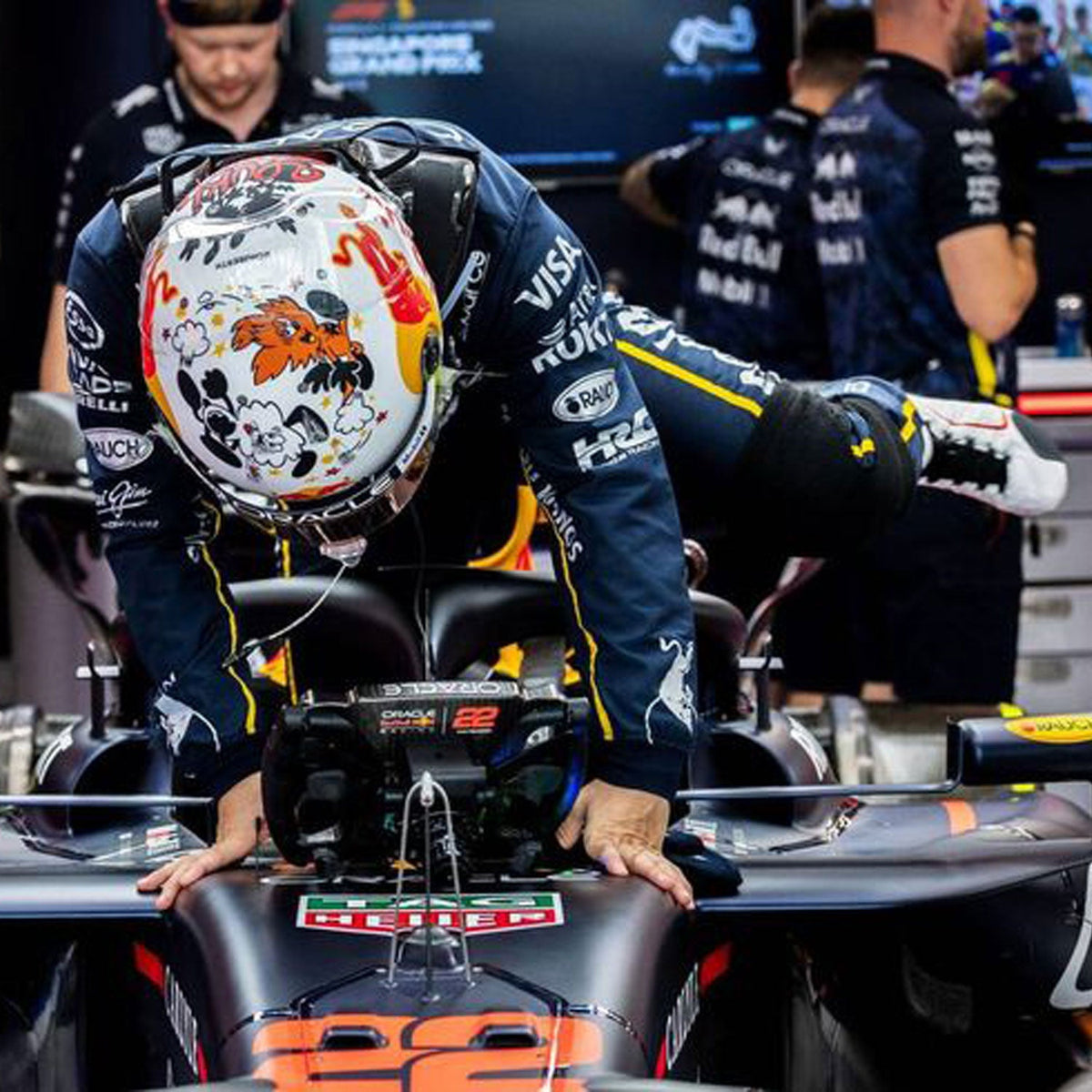 Yuki Tsunoda 2025 F1 Race Costume Red Bull Las Vegas GP and helmet leaning on a Formula 1 car with team logos.