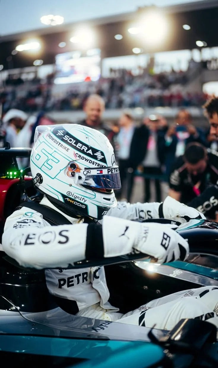 George Russell 2024 Qatar GP Race Gloves F1 Mercedes and helmet sitting in a Formula 1 car with a blurred background of spectators and lights.
