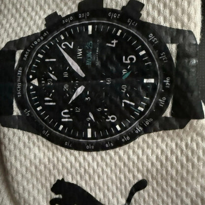 George Russell 2024 Qatar GP Race Gloves F1 Mercedes black wristwatch with a textured black strap, featuring a black dial with white Arabic numerals, white hands, and a black bezel with white tachymeter markings. The watch is photographed flat on a textured off-white fabric background with a black Puma logo printed below.