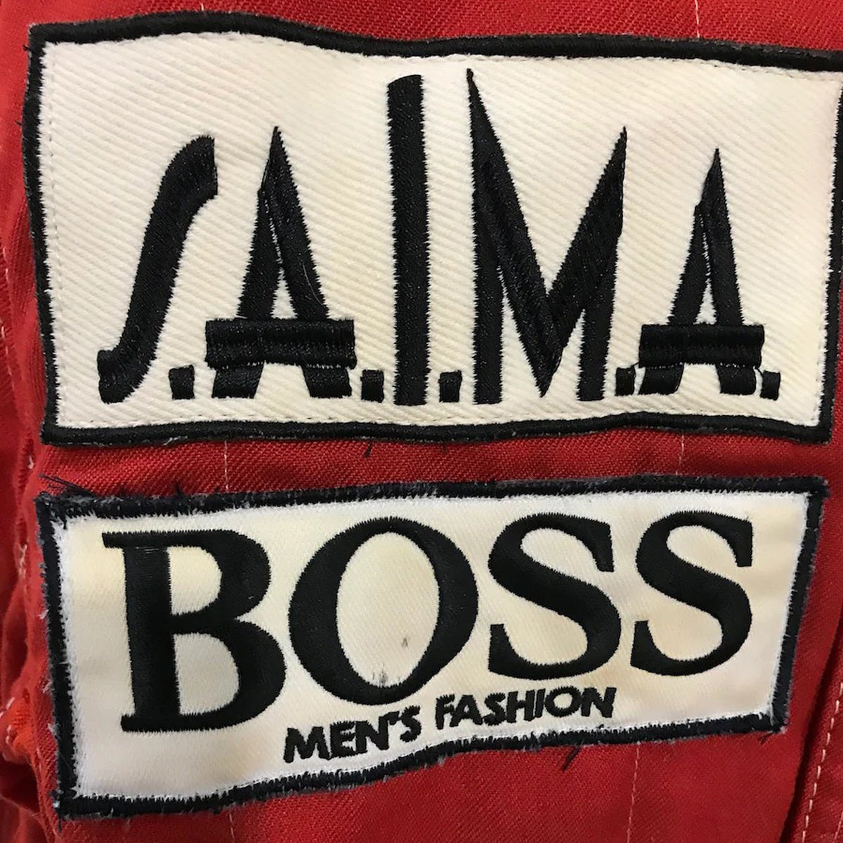 Niki Lauda 1984 F1 Race Costume Replica McLaren World Championship Winning Season Two patches on a red background, one with 'S.A.I.M.A.' and the other with 'BOSS Men's Fashion'.