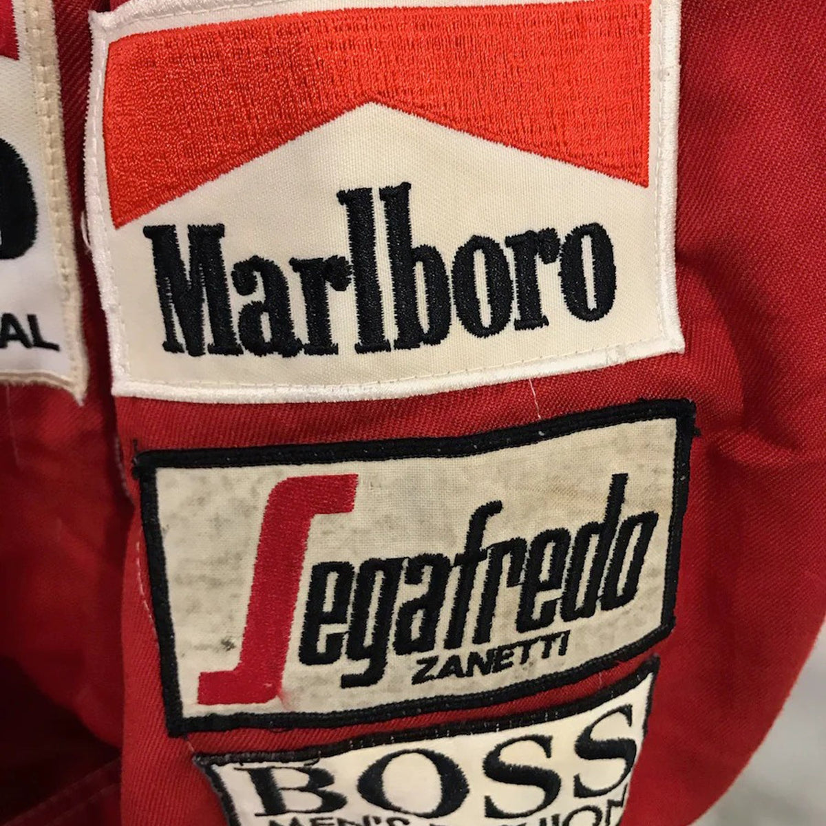 Close-up of a red Niki Lauda 1984 F1 Race Costume Replica McLaren World Championship Winning Season with Marlboro, Segafredo Zanetti, and Boss logos.