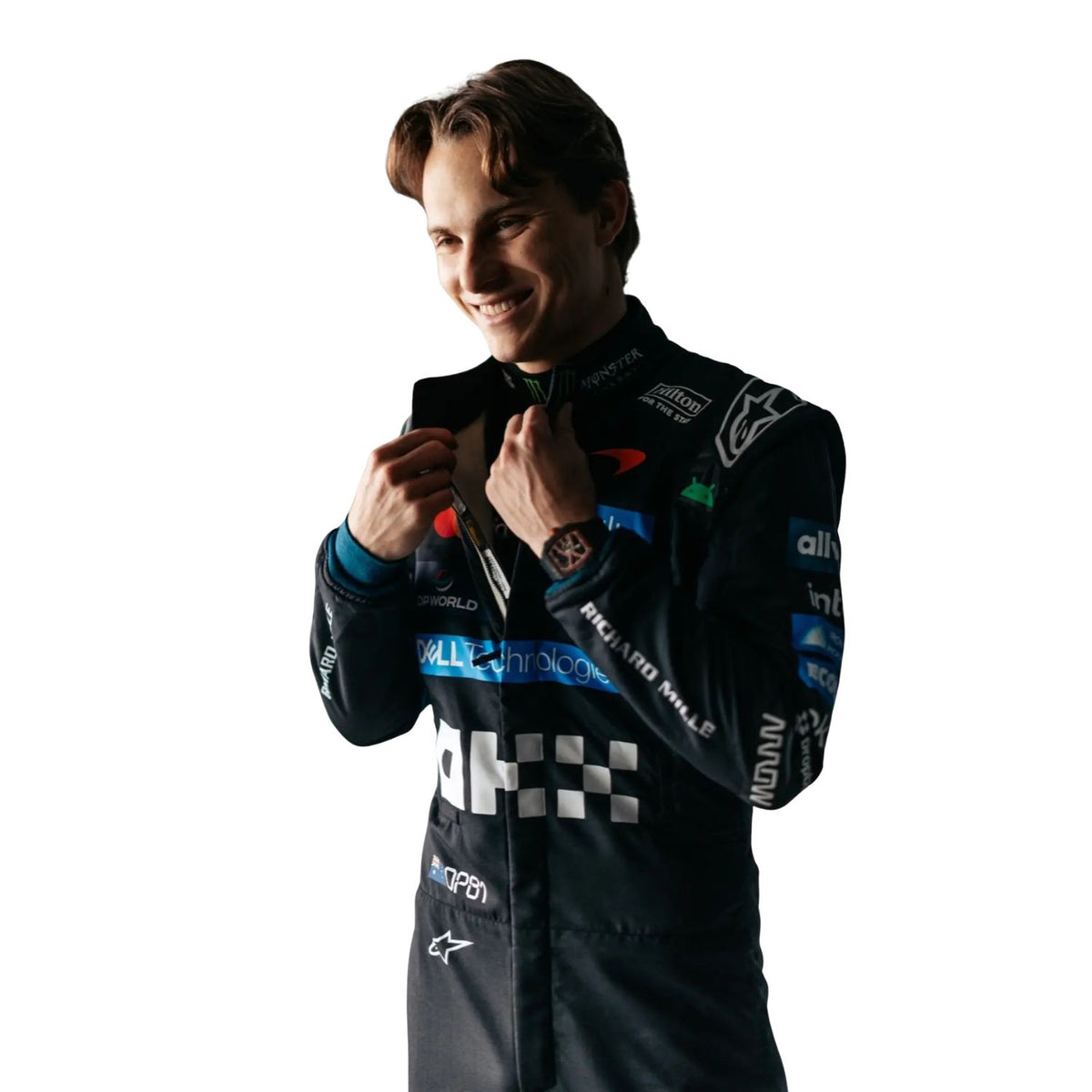 A Oscar Piastri in a dark racing suit with multiple sponsor logos, adjusting the collar of his jacket against a plain white background.