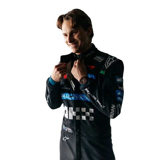 A Oscar Piastri in a dark racing suit with multiple sponsor logos, adjusting the collar of his jacket against a plain white background.