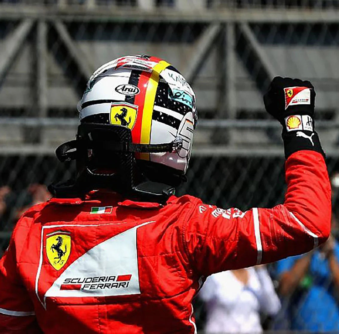 Sebatian Vettel in Ferrari racing suit and helmet celebrating with raised fist wearing 2017 Replica Race Gloves F1 Scuderia Ferrari at a race track.