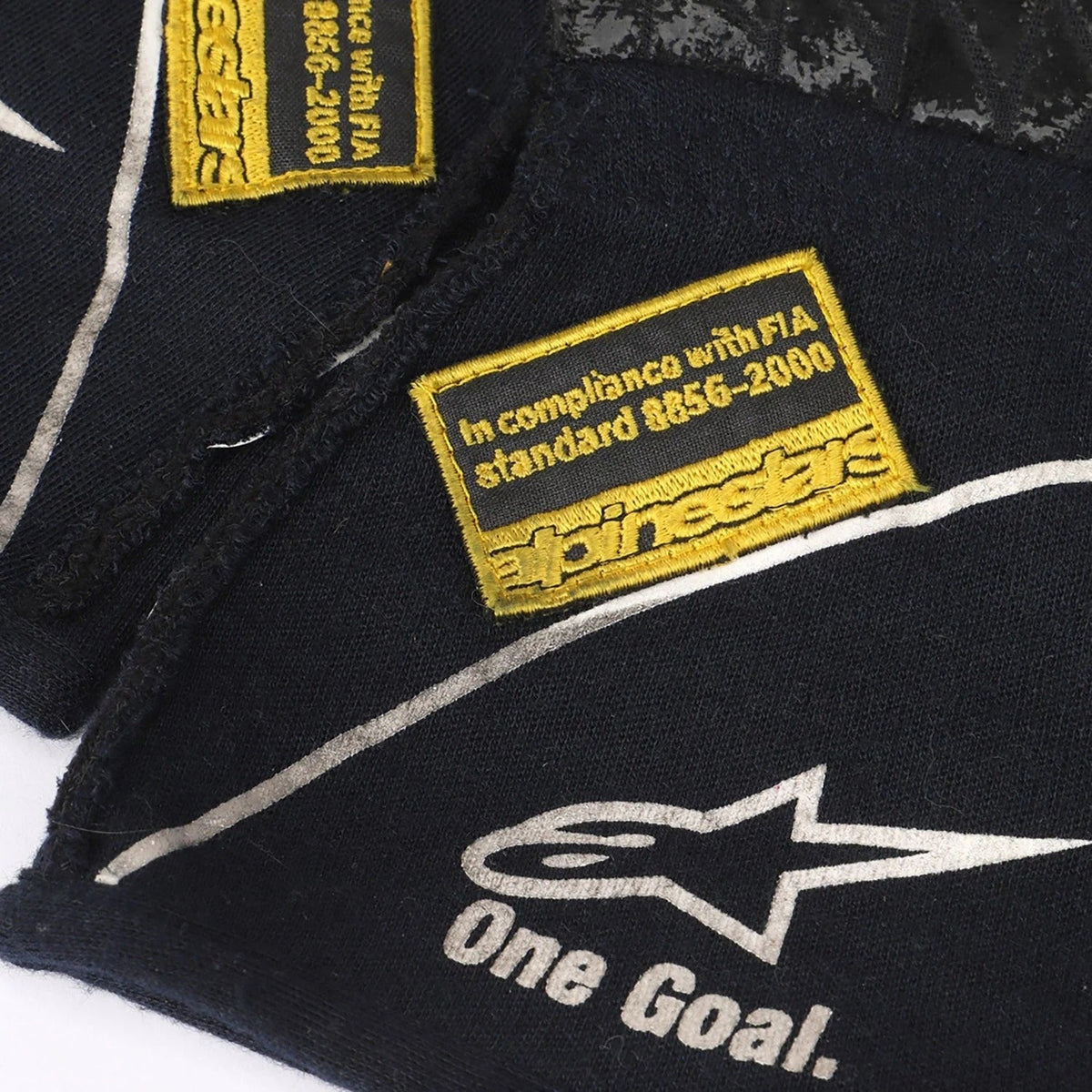 Close-up of a black Valtteri Bottas 2015 Race Gloves Replica F1 Williams Martini with yellow and white text and logos, including 'alpinestars' and 'One Goal.'